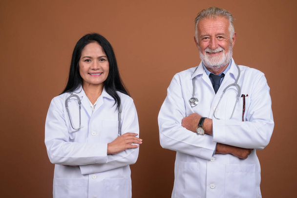 Volwassen multi-etnische paar artsen tegen bruine achtergrond - Foto, afbeelding