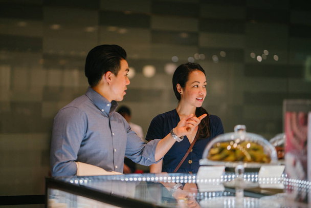  joven pareja asiática china están contemplando una exhibición de pasteles en un centro comercial. Están pensando en comer postres en un fin de semana mientras están en una cita.
. - Foto, imagen