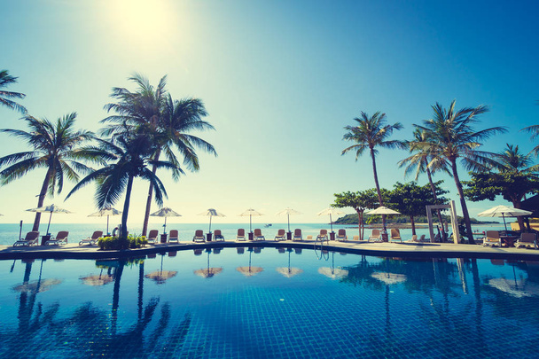 Güzel tropikal plaj ve deniz şemsiyesi ve sandalyesi otel tatil ve tatil için yüzme havuzunda. - Fotoğraf, Görsel