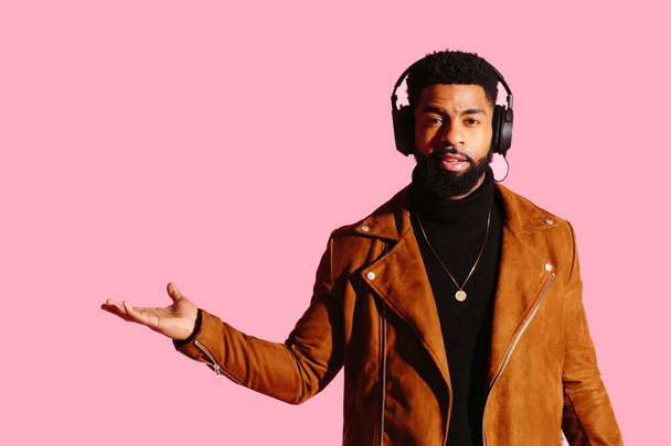 Portrait d'un homme cool avec barbe et écouteurs gesticulant avec sa main isolée sur fond de studio rose
 - Photo, image