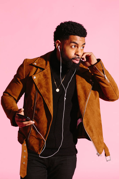 Stylish, handsome and cool African American man with beard, listening to music, texting, isolated on pink studio background - Photo, Image