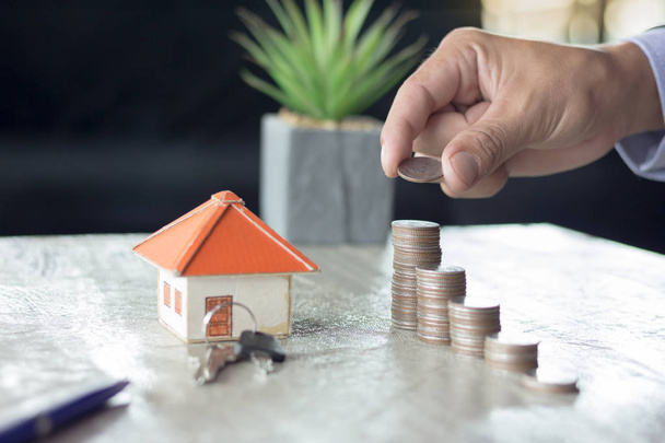 A Person Stacking Coins Near House On Wooden Desk. Property Tax Concept. - Photo, Image