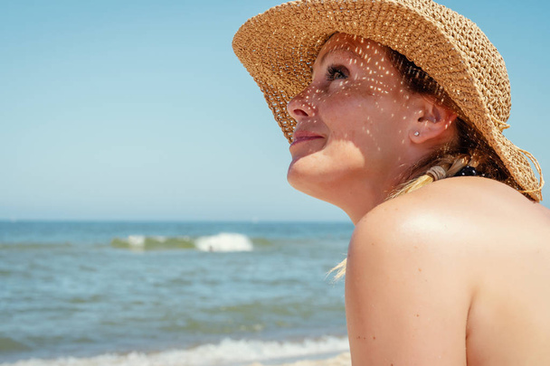 woman in a hat is looking from the beach to the sea in the summer - Foto, afbeelding