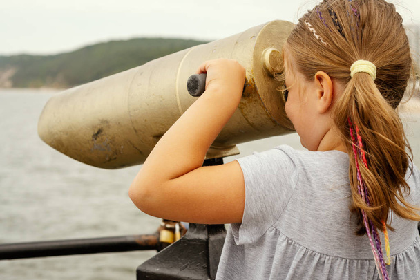 μικρό κορίτσι ψάχνει μέσα από ένα lunete στη θάλασσα το καλοκαίρι - Φωτογραφία, εικόνα