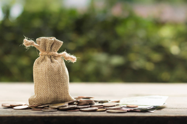 Saving money for future, home, car, education, investment, descendants concept : Money bag with many coins on wood table with green nature as background. Copy space for your text. - Photo, Image