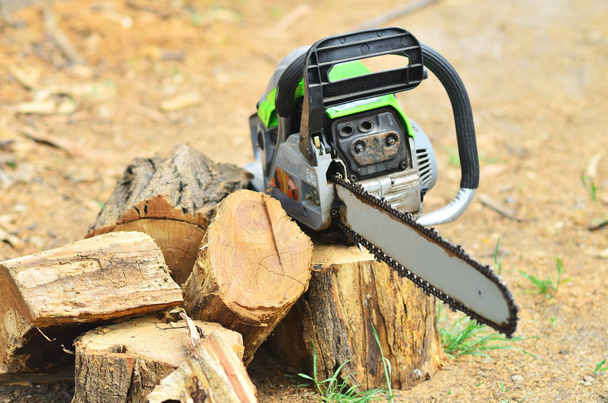 The large working chainsaw is lying on the stump next to the chopped firewood - Foto, Imagen