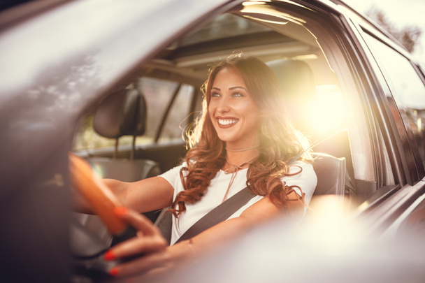 молода усміхнена брюнетка жінка керує новою машиною на заході сонця
 - Фото, зображення