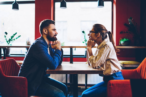 Side view of happy couple in love looking at each other and enjoying leisure time together in stylish cafe interior.Positive boyfriend and cheerful girlfriend communicating during romantic date - Φωτογραφία, εικόνα