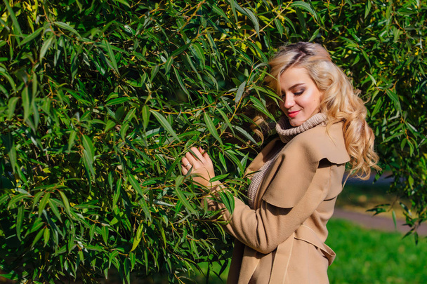 Beautiful elegant blonde woman dressed in a coat standing under the tree in autumn park. Sunny october day. - Fotoğraf, Görsel