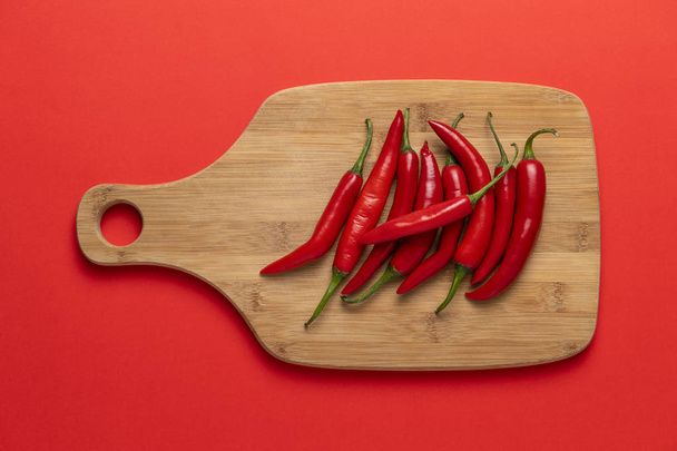 Skupina červené úzké dlouhé pikantní chilli papričkami na dřevěné prkénko na červeném pozadí - Fotografie, Obrázek