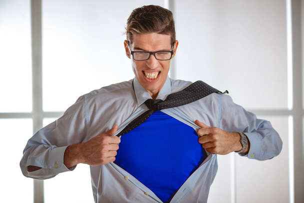 Uomo d'affari arrabbiato strappando camicia aperta ed esponendo costume blu supereroe sotto
 - Foto, immagini