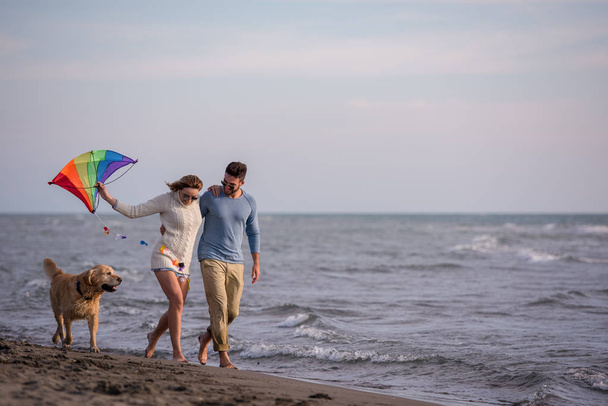 Young Couple having fun playing with a dog and Kite on the beach at autumn day - Foto, Imagem