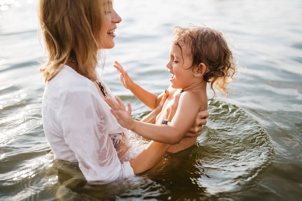 side view of happy mother and daughter standing together in river - Фото, изображение