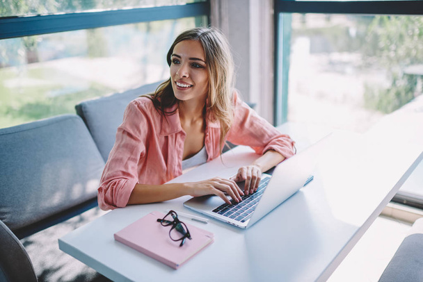 Cheerful female freelancer laughing and looking on side while keyboarding on modern laptop device in search information on internet websites.Positive young woman working remotely at digital netbook - Φωτογραφία, εικόνα
