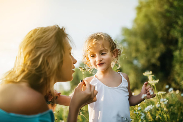 mother sniffing field flowers, smiling daughter looking at mom - Photo, Image