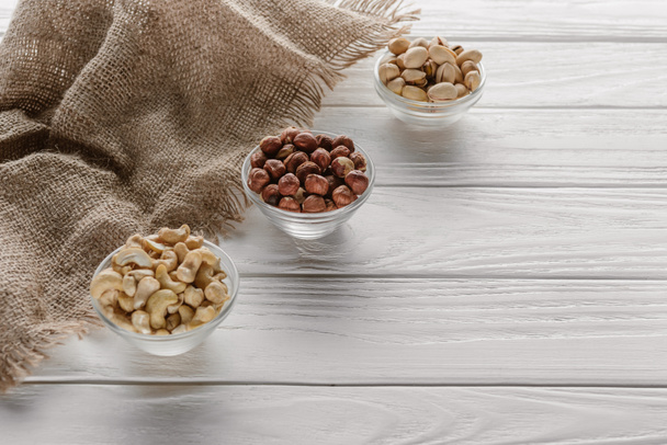 organic nuts in glass bowls on white wooden background - Foto, afbeelding
