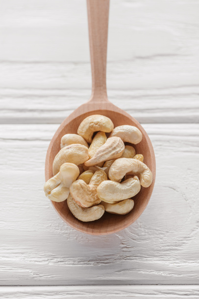 handful of cashew in wooden spoon on white wooden surface - Fotografie, Obrázek