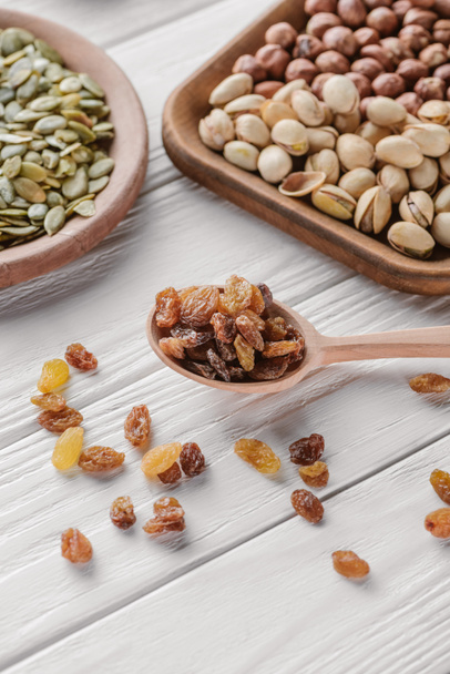 mixed nuts in plates and raisins in spoon on white wooden table - Foto, afbeelding