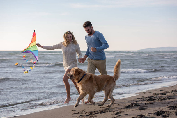 Nuori pari hauskaa leikkii koiran ja Leijan kanssa rannalla syyspäivänä
 - Valokuva, kuva