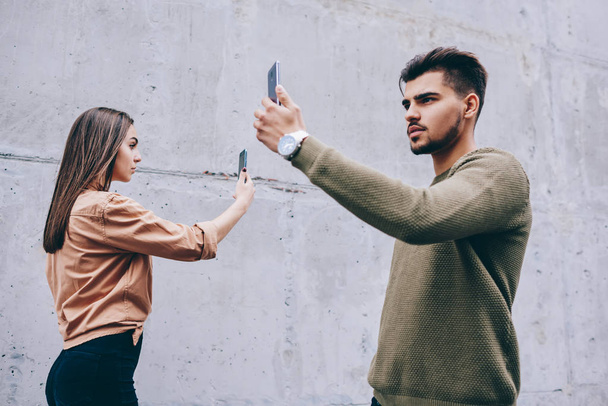 Male and female hipsters walking with smartphones in front of their faces addicted to social networks communication, bloggers shooting video on mobile phone camera while passing each other ignoring - Foto, imagen