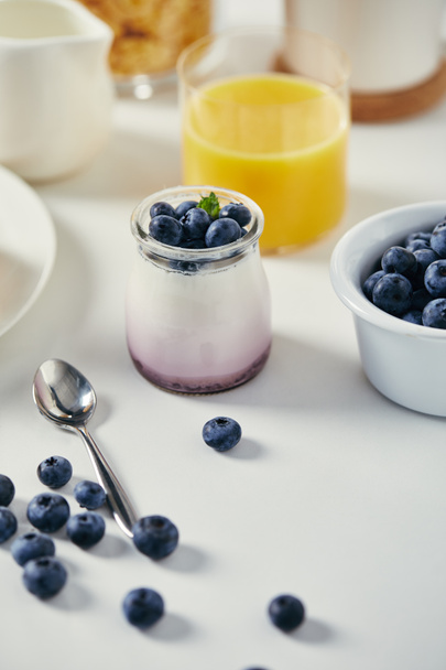 close up view of healthy yogurt with fresh blueberries and glass of juice for breakfast on white tabletop - Photo, Image
