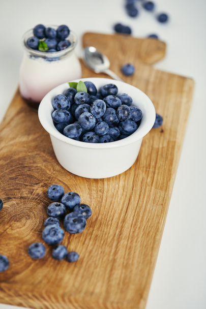 close up view of fresh blueberries and yogurt for breakfast on wooden cutting board - Fotoğraf, Görsel