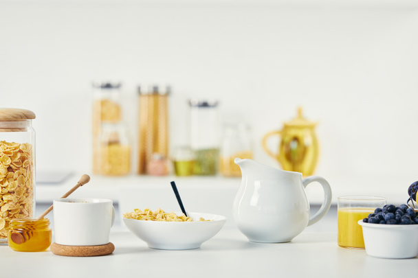 εσωτερικη θέα νιφάδες καλαμποκιού σε μπολ, φλιτζάνι καφέ και κανάτα γάλα για πρωινό σε λευκή επιφάνεια - Φωτογραφία, εικόνα