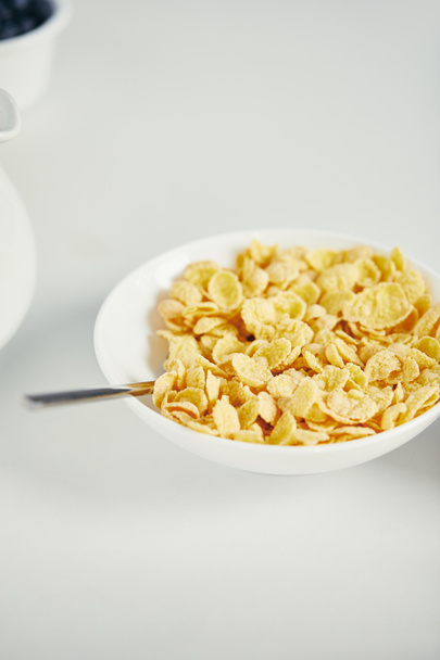 close up view of spoon and corn flakes with milk in bowl for breakfast on white surface - Photo, image
