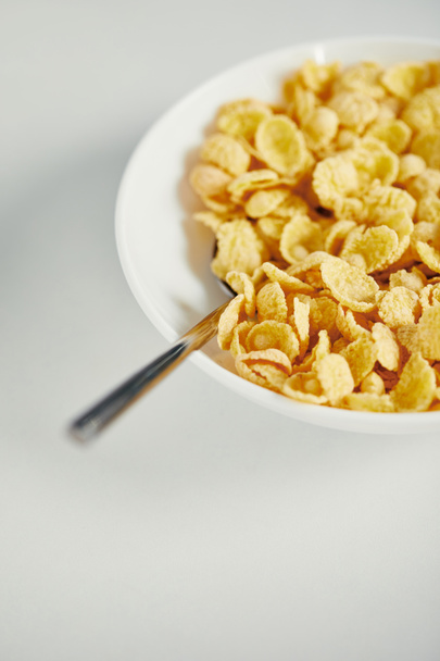 close up view of spoon and corn flakes with milk in bowl for breakfast on white surface - Fotó, kép