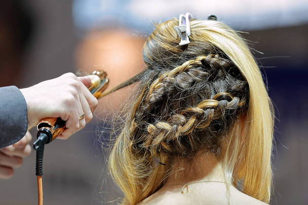 Hairdresser creates hairdo by curling iron in a hair salon - Φωτογραφία, εικόνα