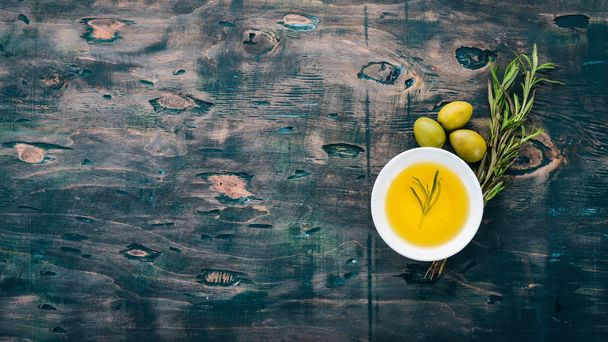Olive oil in a plate and rosemary. On a black wooden background. Free space for text. - Foto, immagini