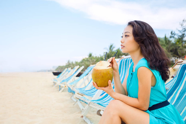Young beautiful asian woman is drinking coconut juice on the tropical sea beach - Foto, imagen