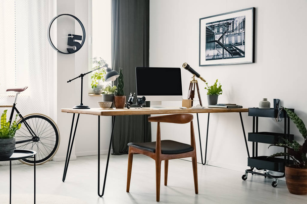 Chair at desk with desktop computer in home office interior with clock and poster. Real photo - 写真・画像