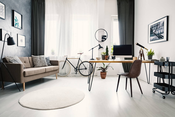 Сучасний інтер'єр домашнього офісу з великим вікном, диваном, велосипедом і столом з комп'ютером. Справжня фотографія
 - Фото, зображення