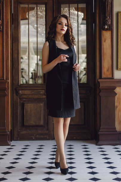 Elegant young woman in black evening dress posing in vintage interior. Fashion shot. - Фото, зображення