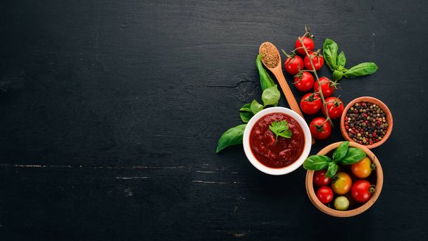 Traditional tomato ketchup sauce. Cherry tomatoes, spices, chili peppers, olive oil, parsley. Top view. On a black wooden background. Free space. - Fotoğraf, Görsel