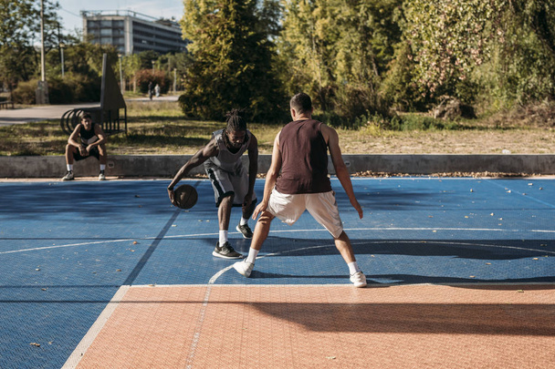 Two handsome men playing basketball outdoors. - Foto, afbeelding