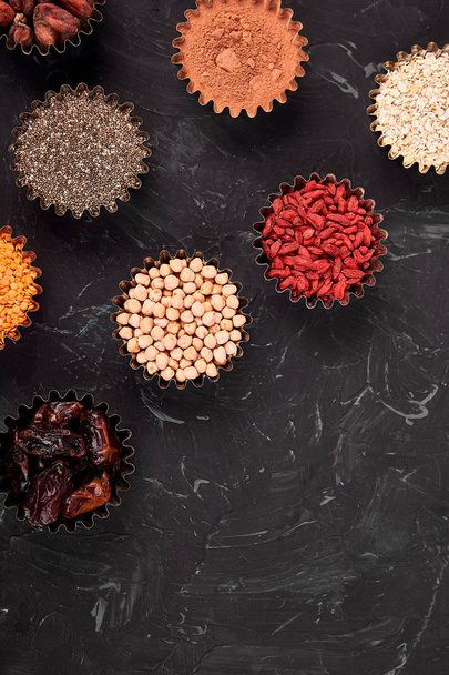 Various superfoods in small bowl on blackbackground. Superfood as chia, raw cocoa bean, goji, chickpeas, lentils. Copy space. Flat lay. - Photo, image