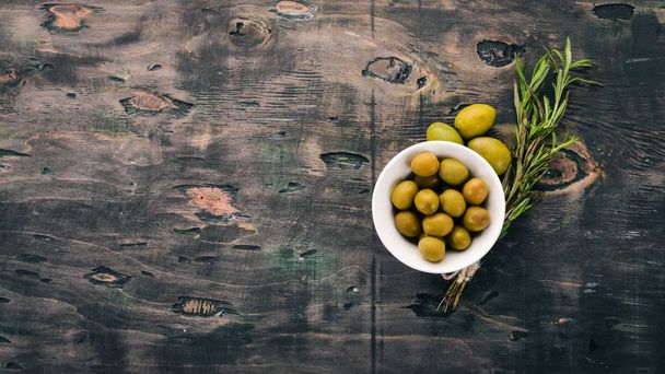 Olives in a plate and rosemary. On a black wooden background. Free space for text. - Foto, afbeelding