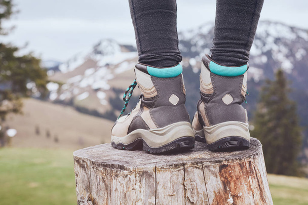 Close up of female classic leather hiking boots wearing by woman standing on stump in mountains - travel and outdoor activities concept - Photo, image