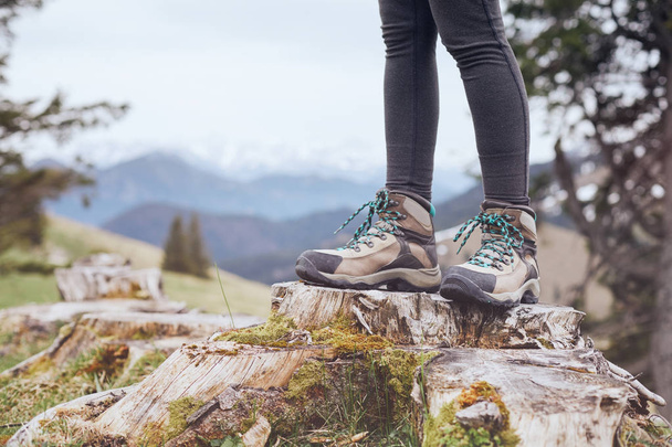 Close up of female classic leather hiking boots wearing by woman standing on stump in mountains - travel and outdoor activities concept - Zdjęcie, obraz