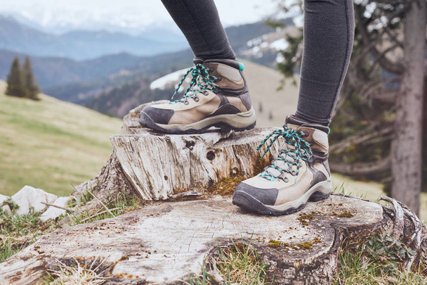 Close up of female classic leather hiking boots wearing by woman standing on stump in mountains - travel and outdoor activities concept - Zdjęcie, obraz
