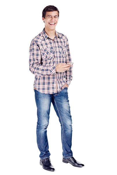 Full body portrait of smiling young man with mobile phone in hand, other hand in pocket wearing metal frame glasses, checkered shirt, blue jeans and black shoes isolated on white background - Φωτογραφία, εικόνα
