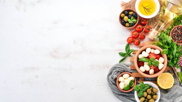 Mozzarella cheese, cherry tomatoes, basil leaves, oil, olives, pepper. Salad caprese On a white wooden table. Free space for text. - Foto, afbeelding