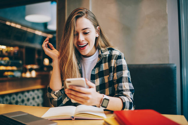 Wonder amazed hipster girl received text message on mobile phone about upcoming discounts, surprised female student chatting with friends and reading schocked news during studying at cafeteria - Fotó, kép