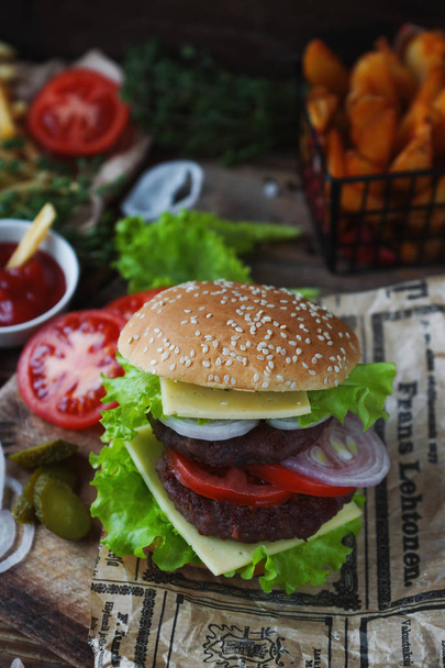 Delicious homemade burger, fried potatoes, fresh tomatoes, lettuce, onions, cheese on rustic wooden table. Fast food set, unhealthy eating concept. Hamburger, french fries, vegetables, selective focus - Fotoğraf, Görsel