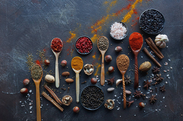 Various indian spices in wooden spoons, herbs and nuts on dark stone table. Colorful italian spices, top view. Organic food, healthy lifestyle, space for text, banner - Foto, imagen