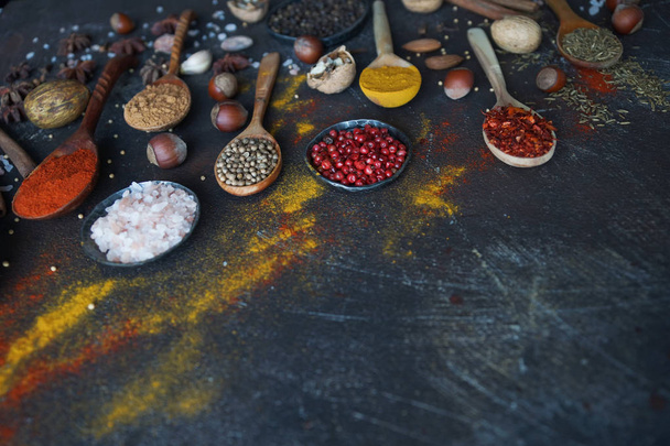 Various indian spices in wooden spoons, herbs and nuts on dark stone table. Colorful italian spices, top view. Organic food, healthy lifestyle, space for text, banner - Fotografie, Obrázek