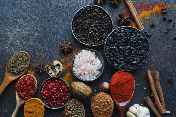 Various indian spices in wooden spoons, herbs and nuts on dark stone table. Colorful italian spices, top view. Organic food, healthy lifestyle, space for text, banner - Photo, Image