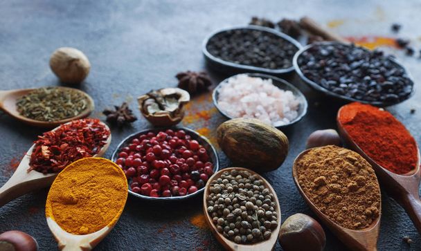 Various indian spices in wooden spoons, herbs and nuts on dark stone table. Colorful italian spices, top view. Organic food, healthy lifestyle, space for text, banner - Φωτογραφία, εικόνα